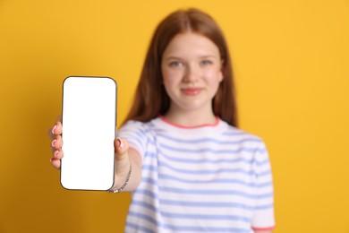 Photo of Beautiful teenage girl showing smartphone with blank screen on yellow background, selective focus. Mockup for design
