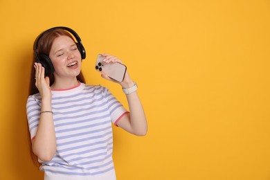 Photo of Happy teenage girl in headphones with smartphone singing on yellow background. Space for text