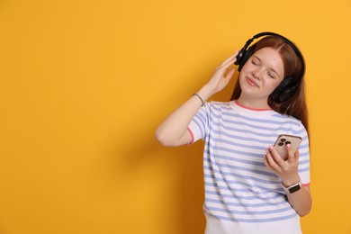 Photo of Beautiful teenage girl in headphones with smartphone on yellow background. Space for text