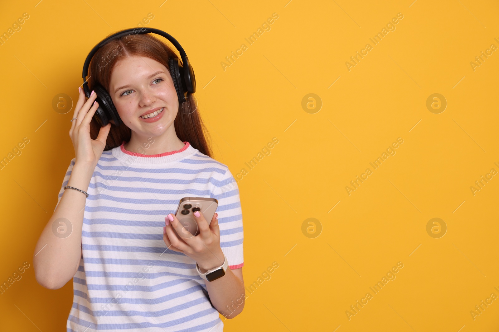Smiling teenage girl in headphones with smartphone on yellow background. Space for text Photo of Smiling teenage girl in headphones with smartphone on yellow background. Space for text
