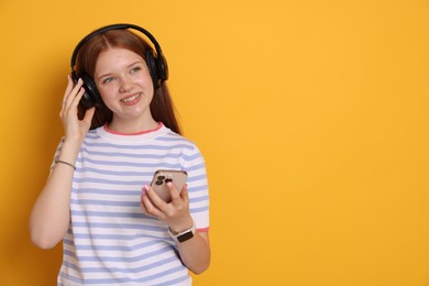 Photo of Smiling teenage girl in headphones with smartphone on yellow background. Space for text