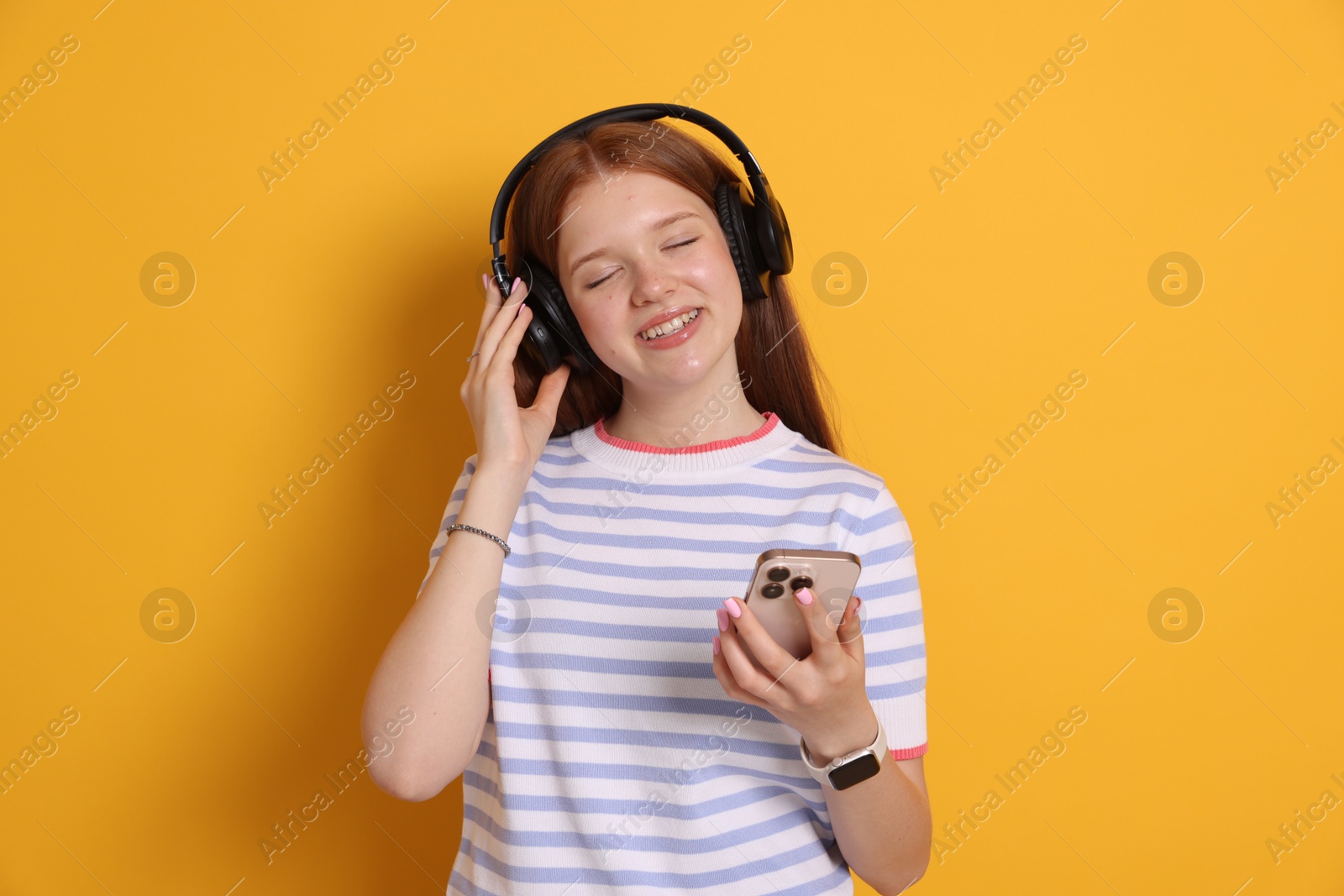 Smiling teenage girl in headphones with smartphone on yellow background Photo of Smiling teenage girl in headphones with smartphone on yellow background
