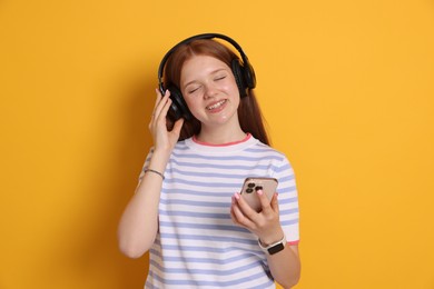 Photo of Smiling teenage girl in headphones with smartphone on yellow background