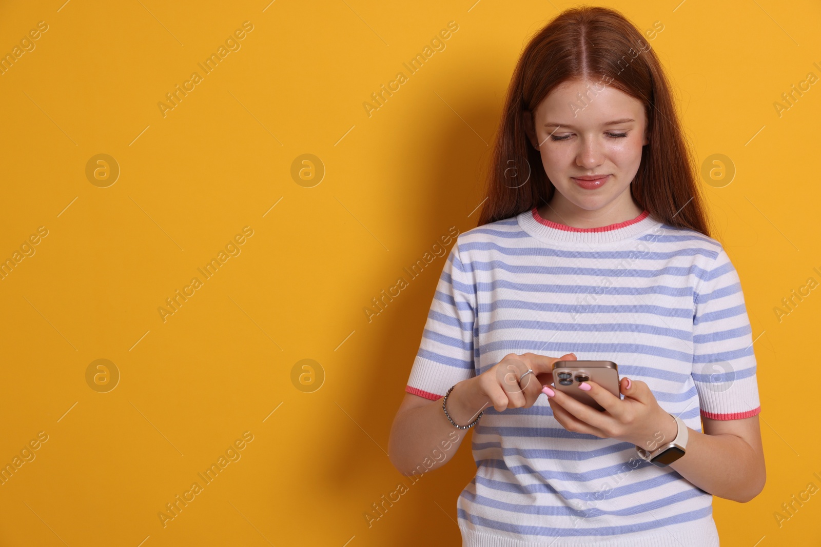 Beautiful teenage girl using smartphone on yellow background. Space for text Photo of Beautiful teenage girl using smartphone on yellow background. Space for text