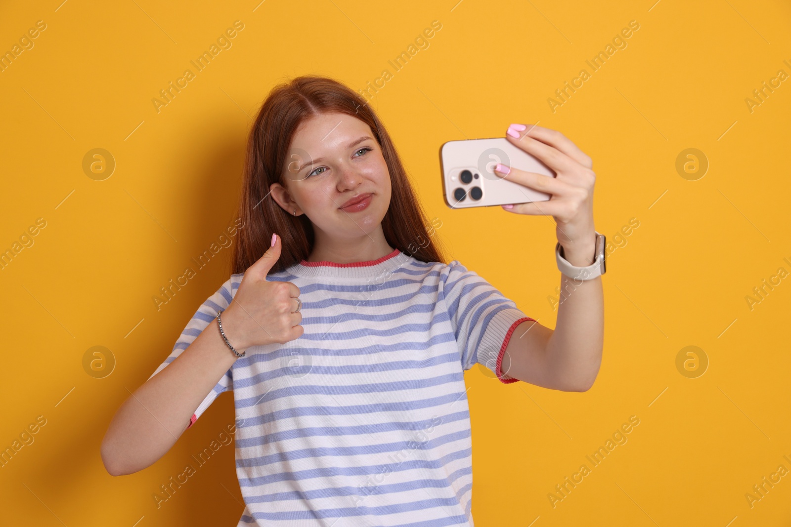 Beautiful teenage girl taking selfie by smartphone and showing thumbs up on yellow background Photo of Beautiful teenage girl taking selfie by smartphone and showing thumbs up on yellow background