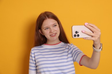 Photo of Smiling teenage girl taking selfie by smartphone on yellow background