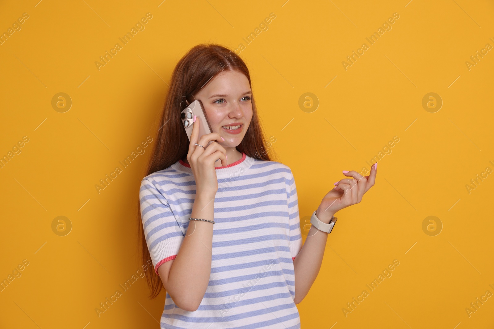 Smiling teenage girl talking by smartphone on yellow background Photo of Smiling teenage girl talking by smartphone on yellow background