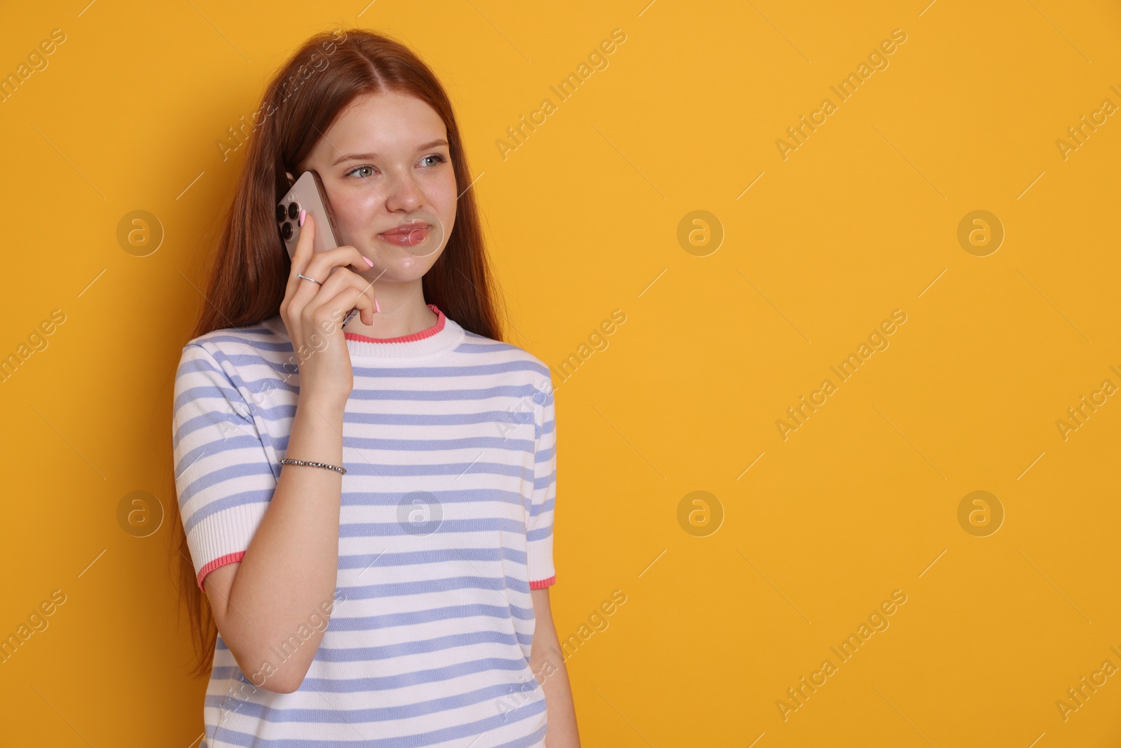 Beautiful teenage girl talking by smartphone on yellow background. Space for text Photo of Beautiful teenage girl talking by smartphone on yellow background. Space for text