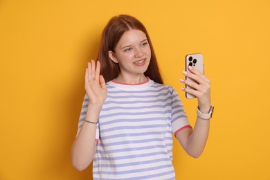 Photo of Smiling teenage girl having videocall by smartphone on yellow background
