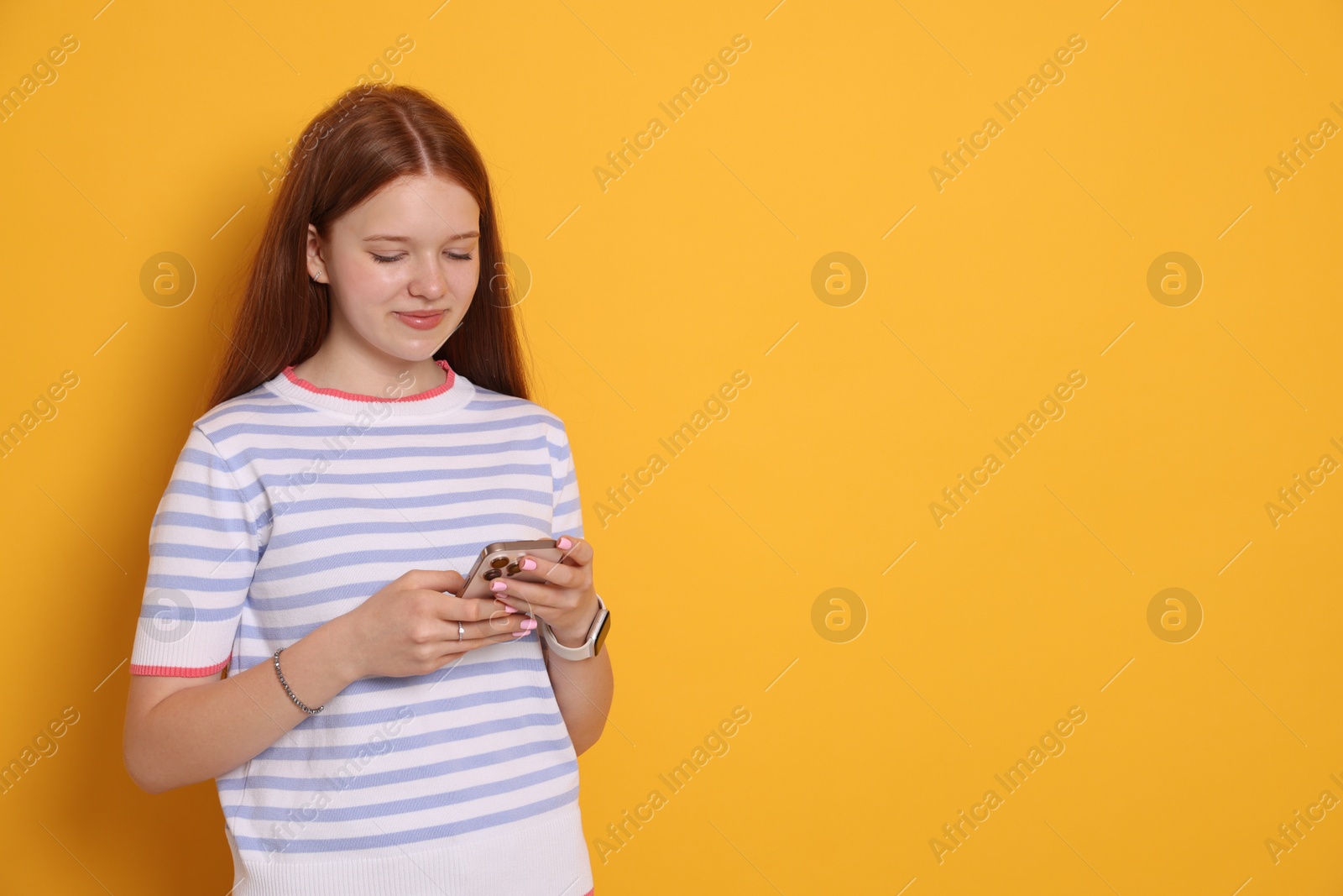 Beautiful teenage girl using smartphone on yellow background. Space for text Photo of Beautiful teenage girl using smartphone on yellow background. Space for text