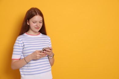 Photo of Beautiful teenage girl using smartphone on yellow background. Space for text