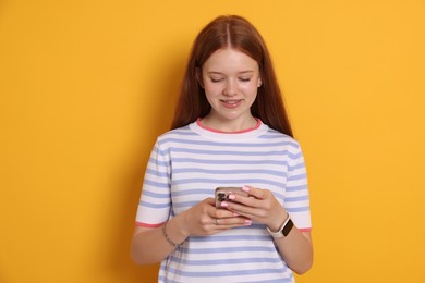 Photo of Smiling teenage girl using smartphone on yellow background