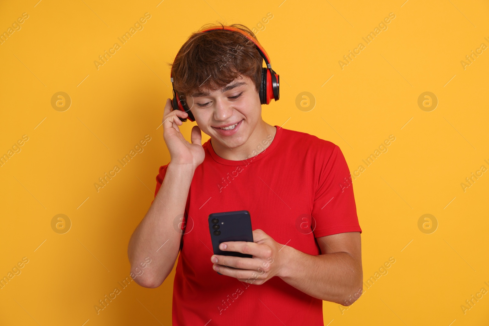 Photo of Smiling teenage boy in headphones with smartphone on yellow background