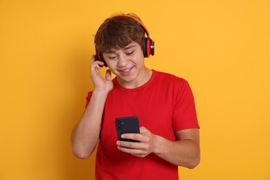Photo of Smiling teenage boy in headphones with smartphone on yellow background
