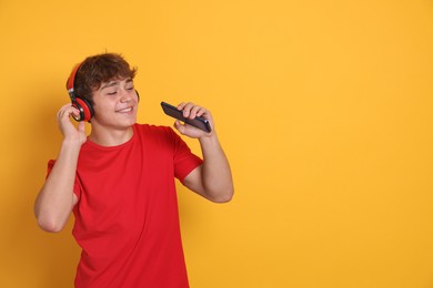 Photo of Smiling teenage boy in headphones with smartphone on yellow background. Space for text
