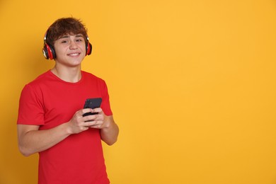 Photo of Smiling teenage boy in headphones with smartphone on yellow background. Space for text