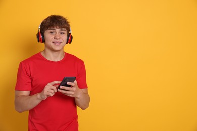 Photo of Smiling teenage boy in headphones with smartphone on yellow background. Space for text