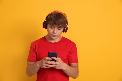 Photo of Teenage boy in headphones using smartphone on yellow background