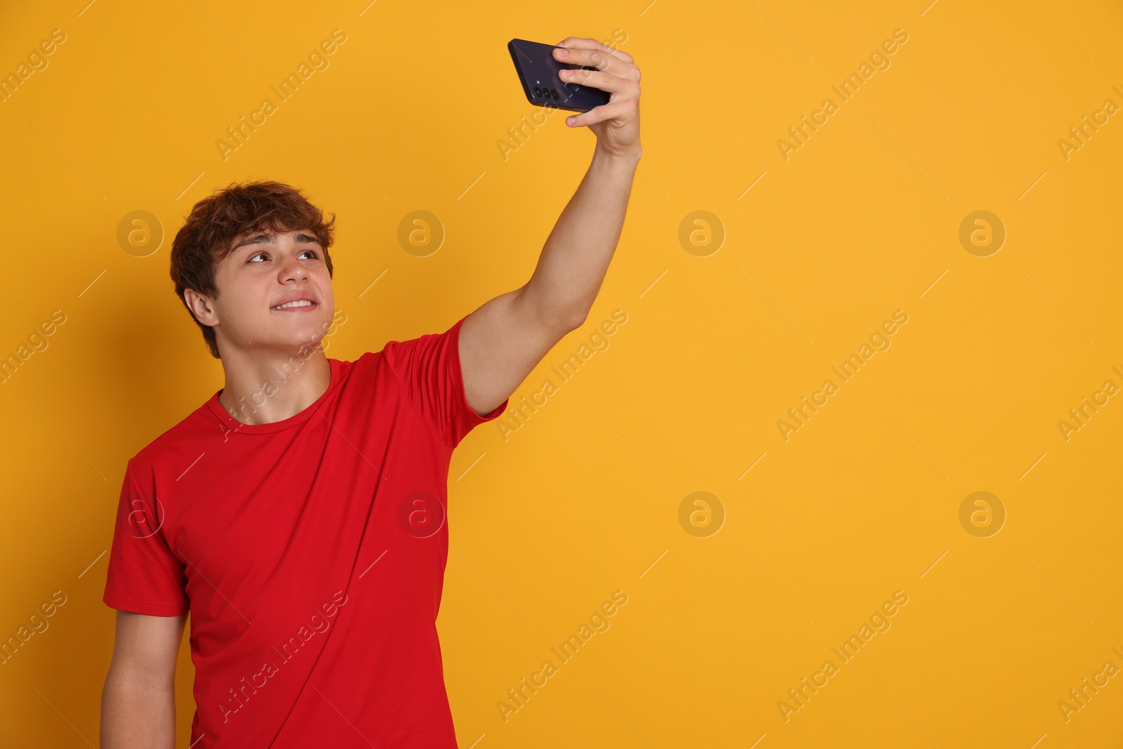 Photo of Smiling teenage boy taking selfie by smartphone on yellow background. Space for text