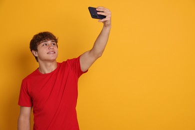 Photo of Smiling teenage boy taking selfie by smartphone on yellow background. Space for text
