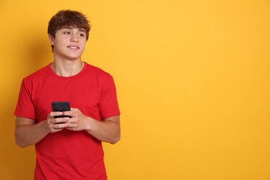 Photo of Smiling teenage boy with smartphone on yellow background. Space for text