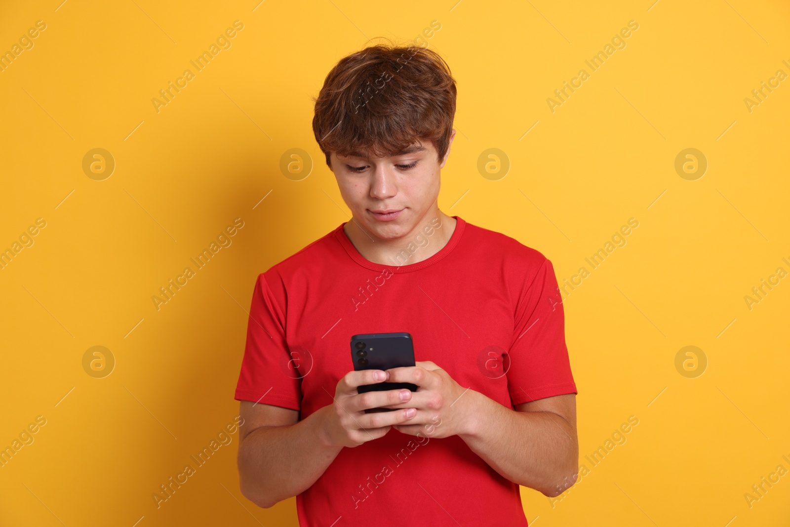 Photo of Teenage boy using smartphone on yellow background