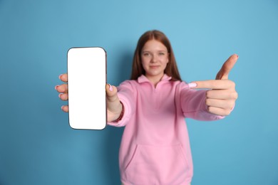 Photo of Beautiful teenage girl showing smartphone with blank screen on light blue background, selective focus. Mockup for design