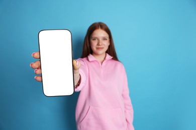 Photo of Beautiful teenage girl showing smartphone with blank screen on light blue background, selective focus. Mockup for design