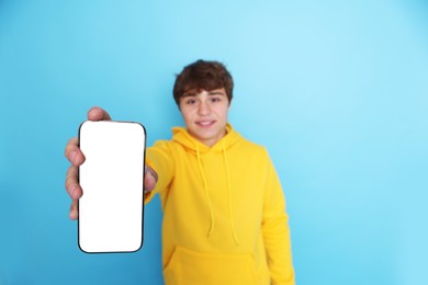 Photo of Smiling teenage boy showing smartphone with blank screen on light blue background, selective focus. Mockup for design