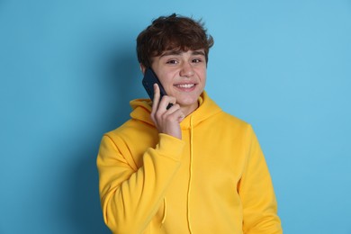 Photo of Portrait of smiling teenage boy talking by smartphone on light blue background