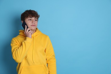 Photo of Teenage boy talking by smartphone on light blue background. Space for text