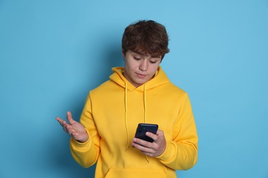Photo of Teenage boy with smartphone on light blue background