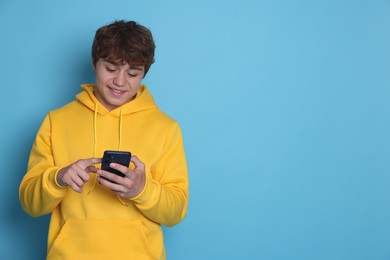 Photo of Smiling teenage boy using smartphone on light blue background. Space for text