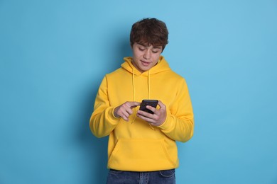 Photo of Teenage boy using smartphone on light blue background