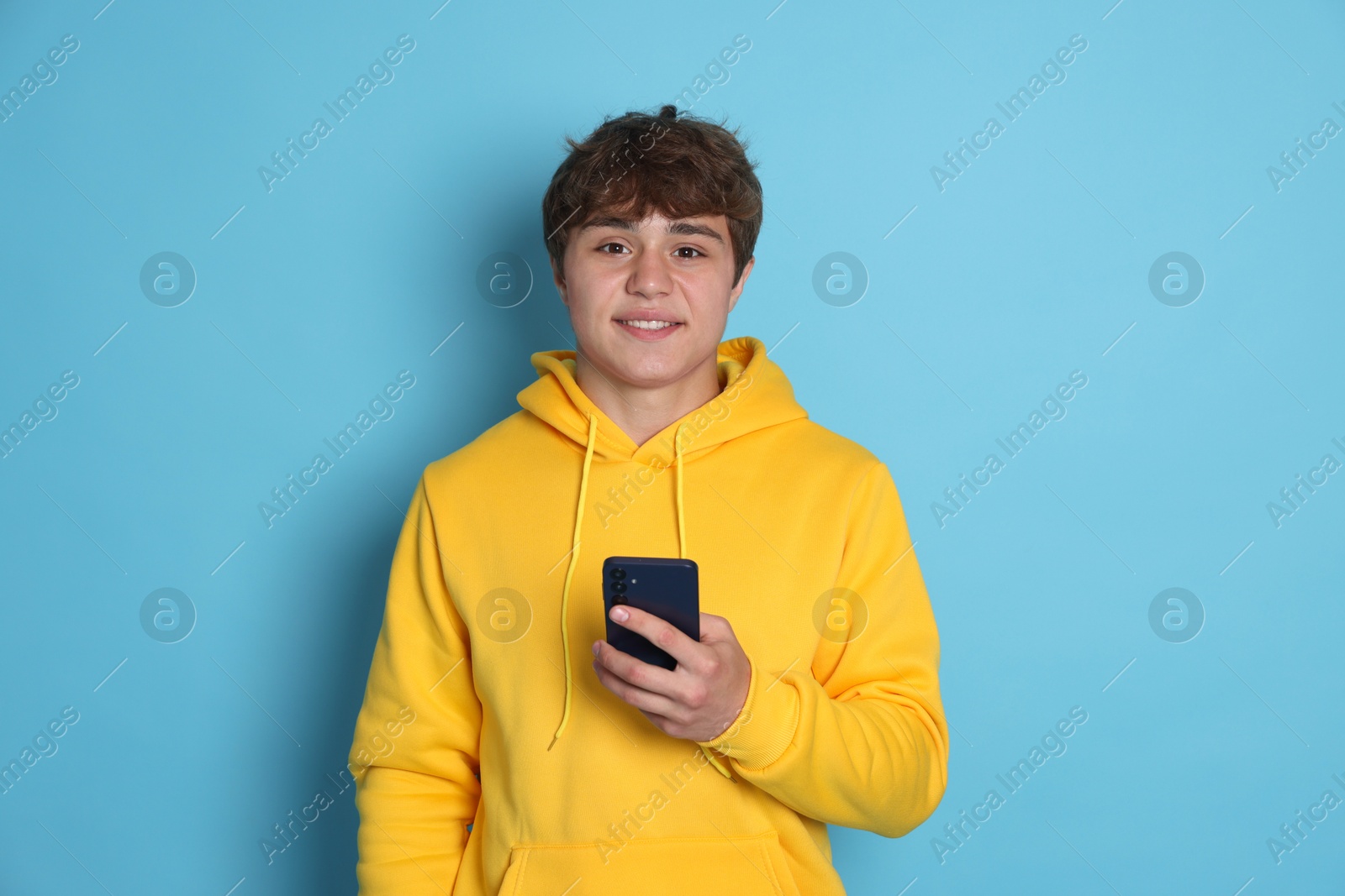 Photo of Portrait of smiling teenage boy with smartphone on light blue background