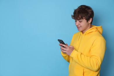 Photo of Smiling teenage boy using smartphone on light blue background. Space for text