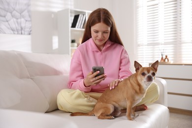 Photo of Beautiful teenage girl with smartphone and dog on sofa at home