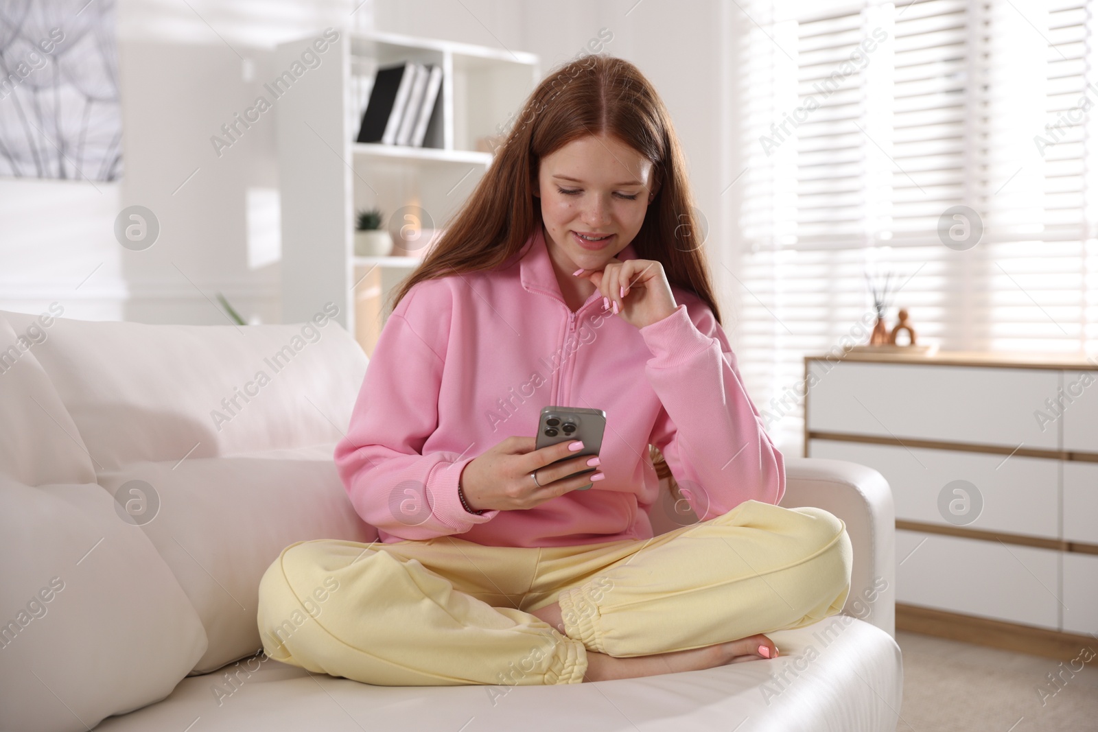 Smiling teenage girl using smartphone on sofa at home Photo of Smiling teenage girl using smartphone on sofa at home
