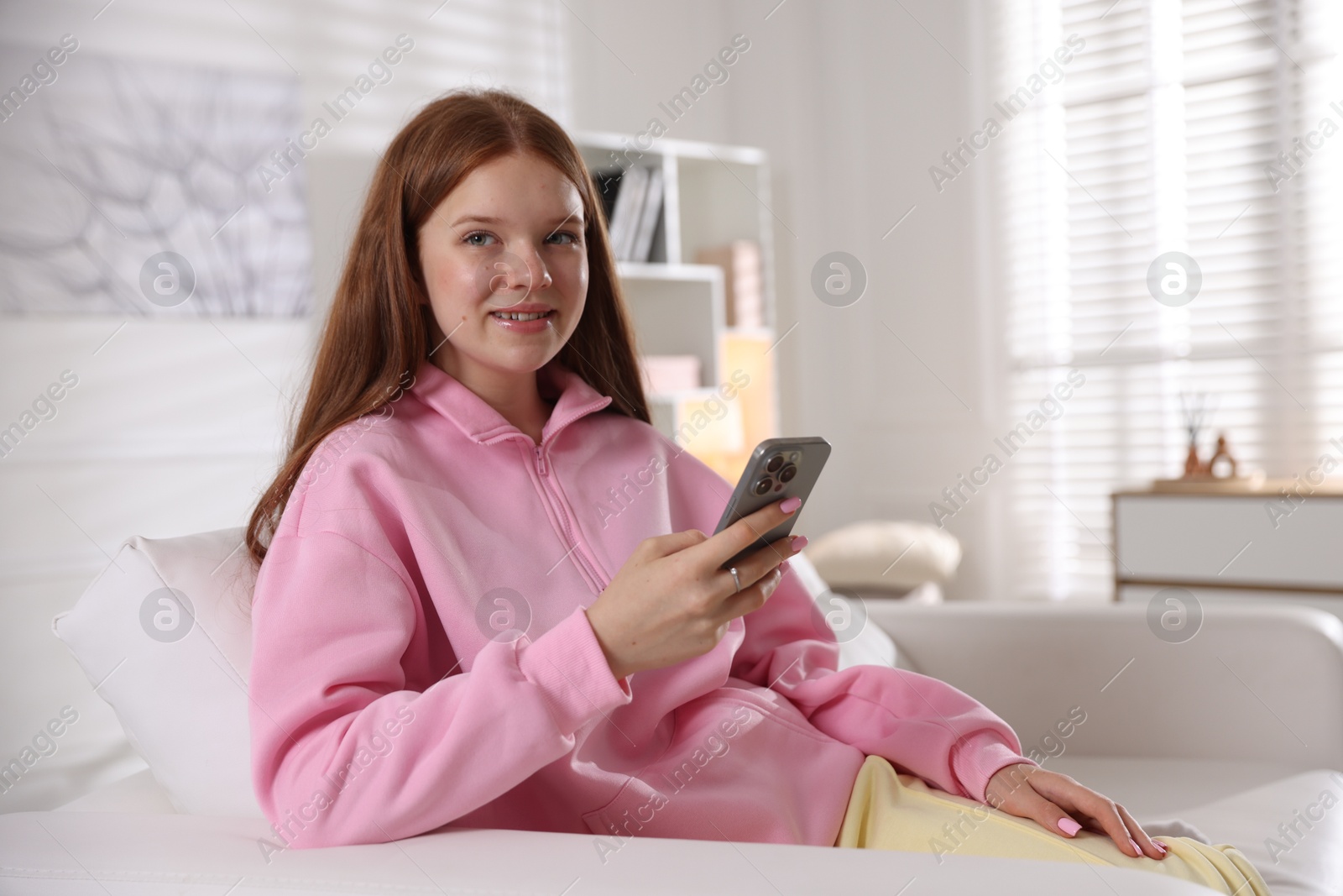 Smiling teenage girl with smartphone on sofa at home Photo of Smiling teenage girl with smartphone on sofa at home