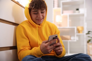 Photo of Smiling teenage boy using smartphone at home