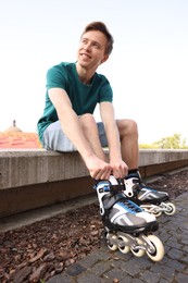 Photo of Happy man putting on roller skates outdoors