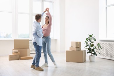 Photo of Happy young couple dancing and cardboard boxes at home. Moving day