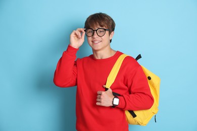 Photo of Smiling teenage boy in glasses with book and backpack on light blue background