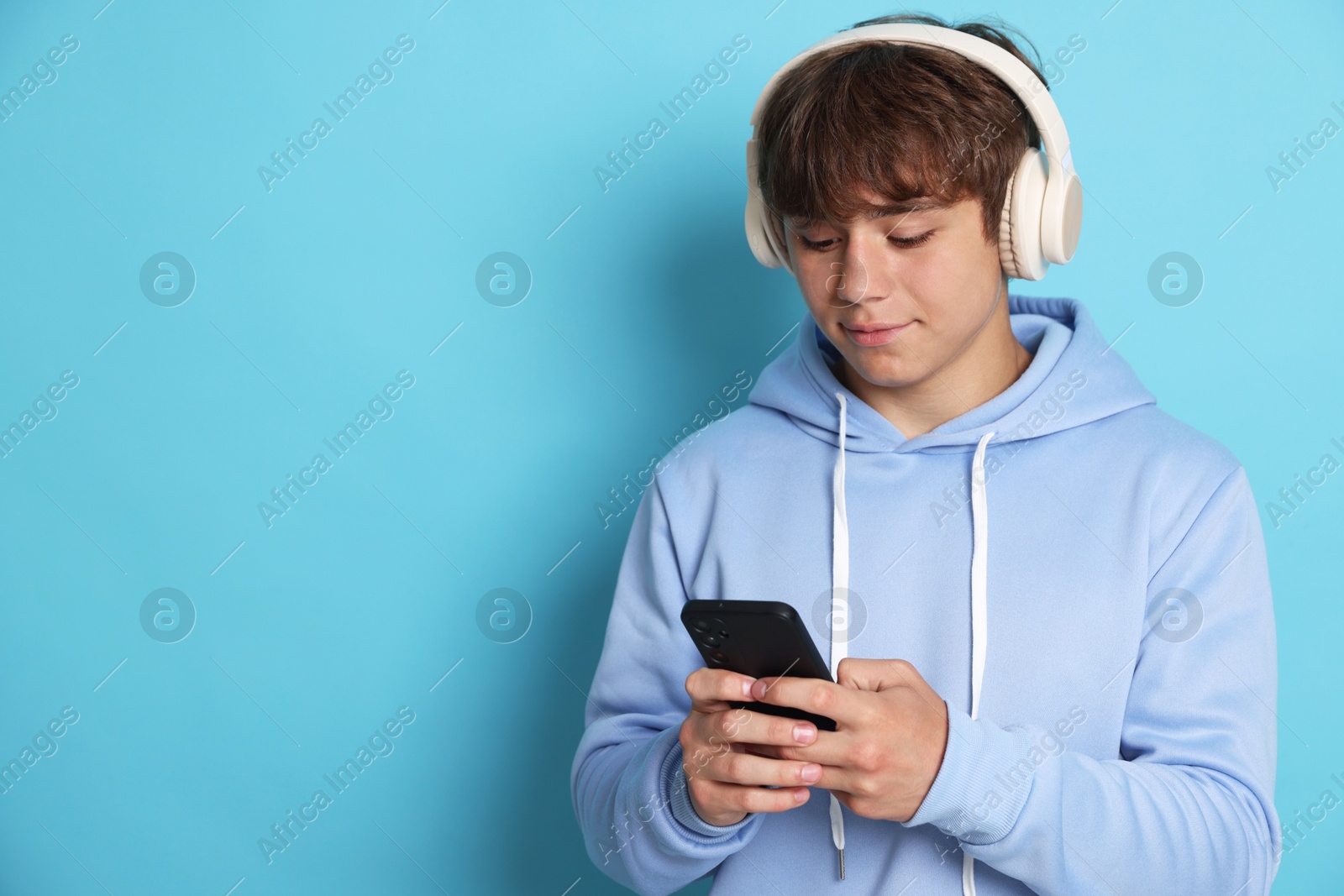 Cute teenage boy in headphones with smartphone on light blue background. Space for text Photo of Cute teenage boy in headphones with smartphone on light blue background. Space for text