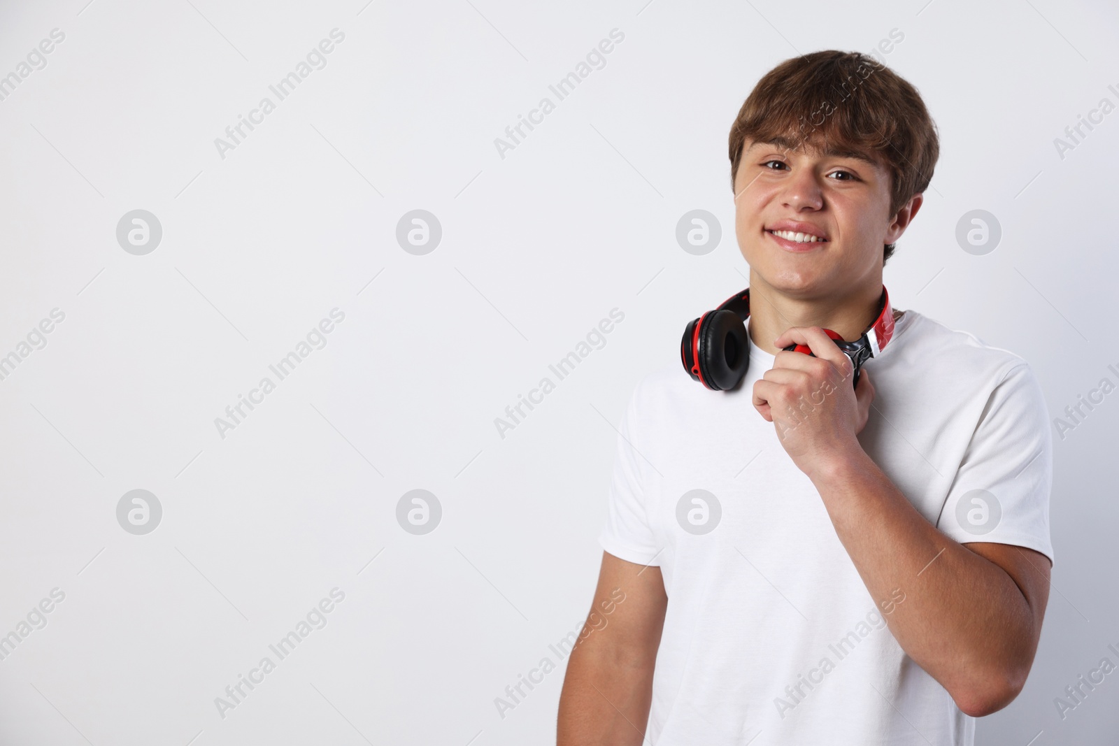 Photo of Portrait of smiling teenage boy with headphones on light grey background. Space for text