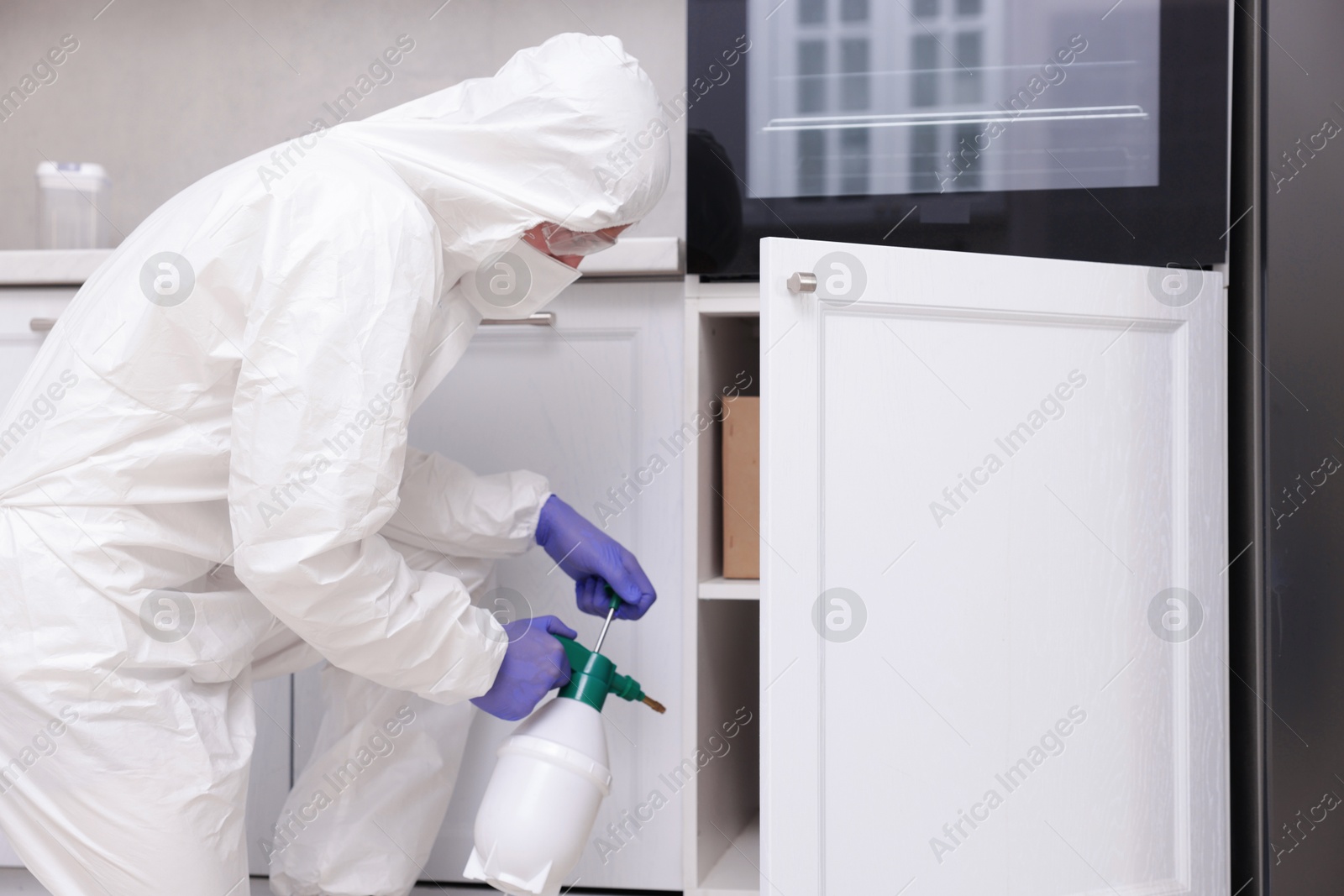 Photo of Pest control worker in protective suit spraying insecticide at home