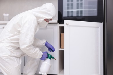 Photo of Pest control worker in protective suit spraying insecticide at home