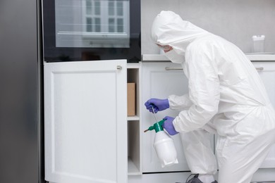 Photo of Pest control worker in protective suit spraying insecticide at home
