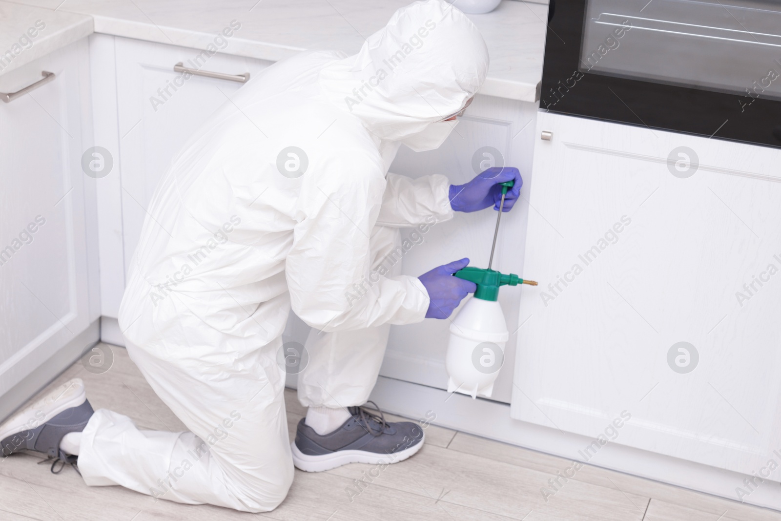 Photo of Pest control worker in protective suit spraying insecticide at home