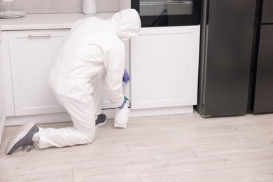 Photo of Pest control worker in protective suit spraying insecticide at home